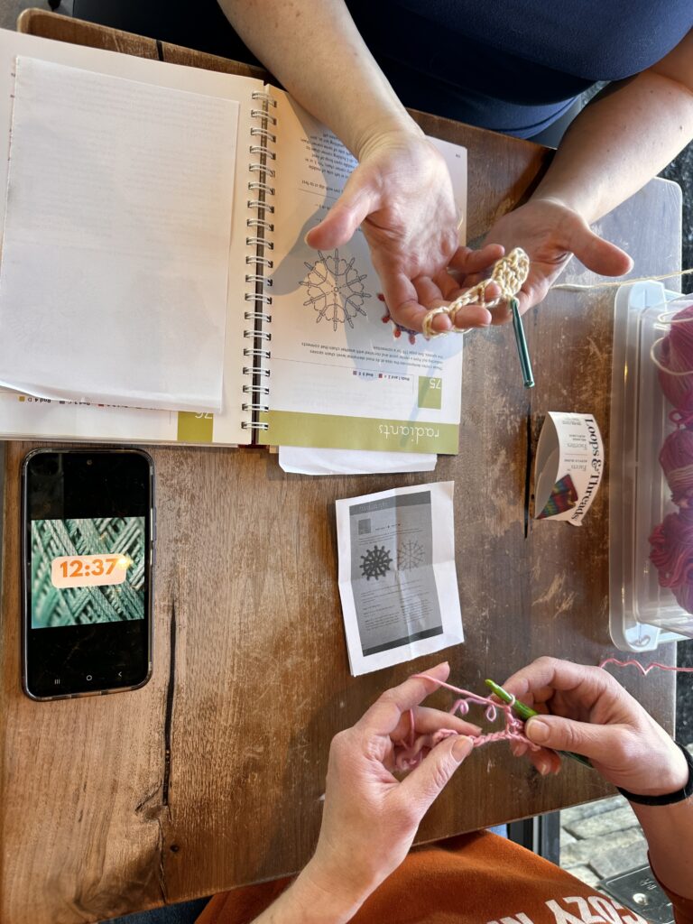 Two women crocheting together in a coffee shop