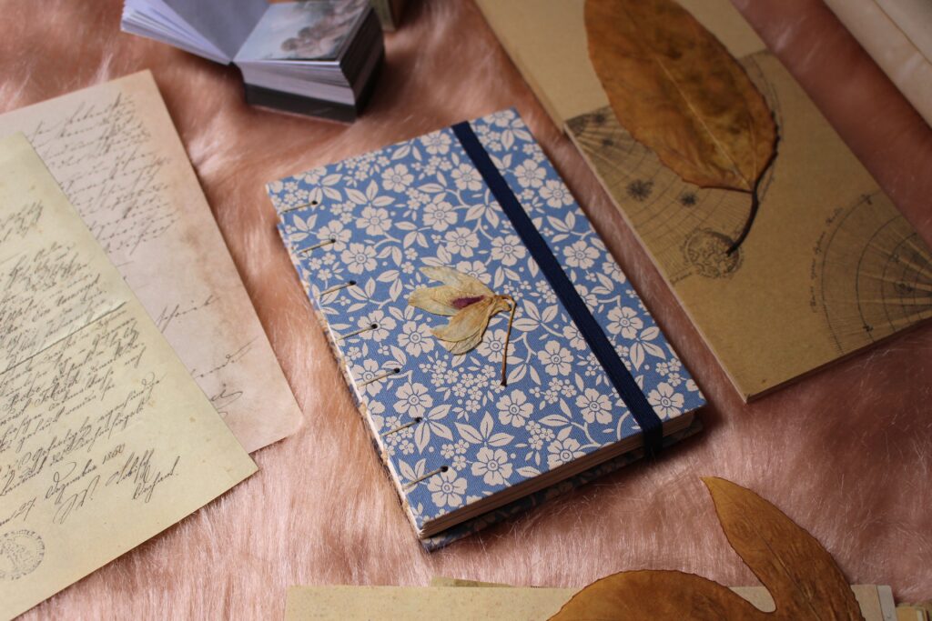 Artistic flat lay of a journal with floral cover, dried leaves, and handwritten letters.